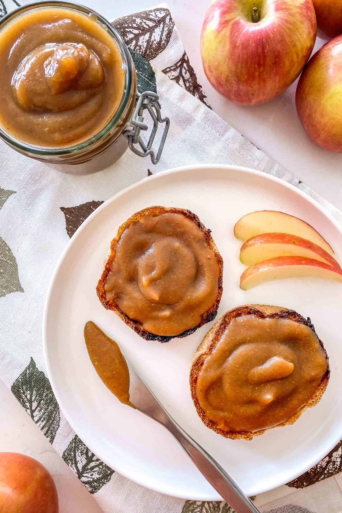 English muffin on white plate with apple spread on top and knife on the side.
