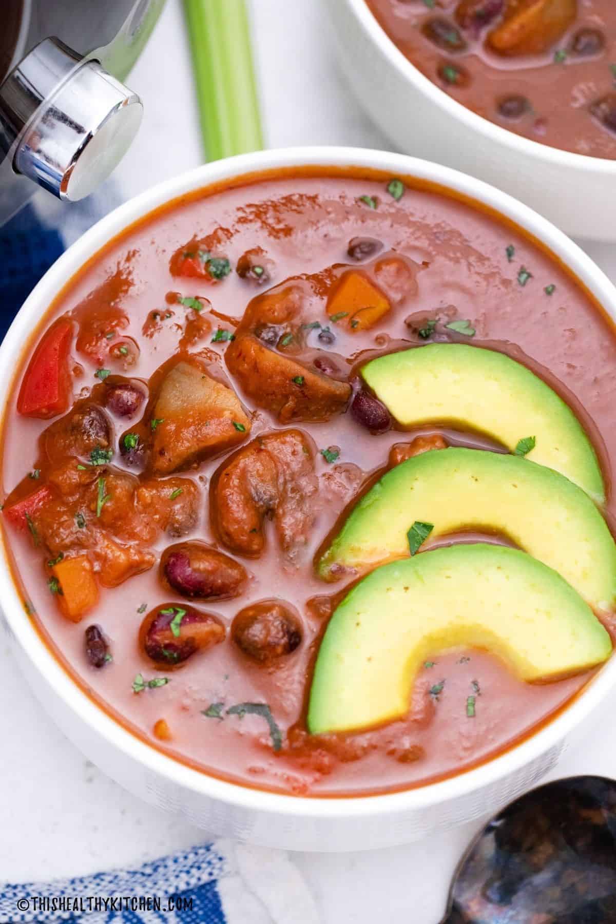 White bowl of tomato bean soup with avocado slices on top.