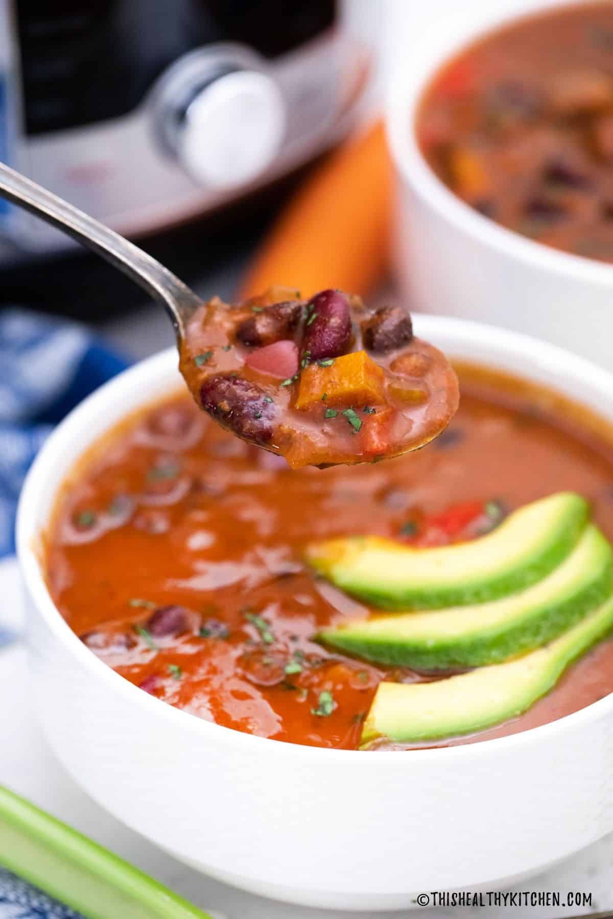 Spoonful of bean soup being held above bowl.