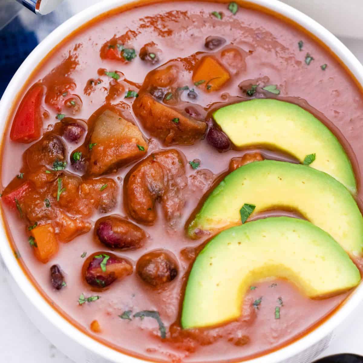 White bowl of tomato bean soup with avocado slices on top.