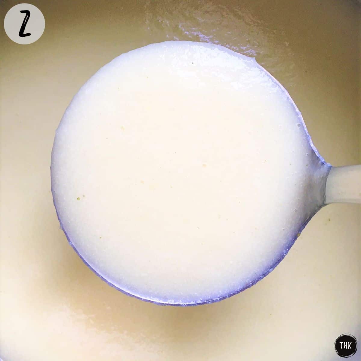Scoop of cauliflower soup in ladle being held over pot.