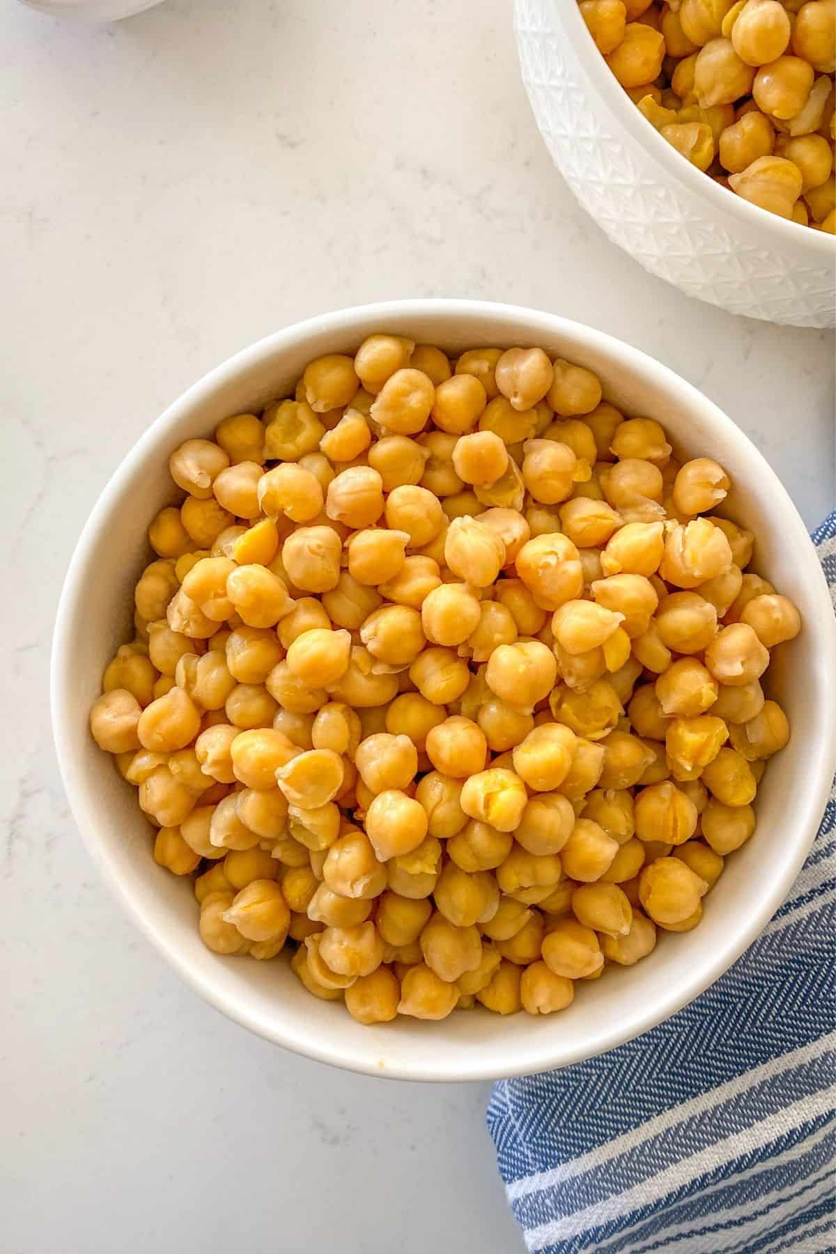 White bowl filled with cooked chickpeas and blue towel beside it.