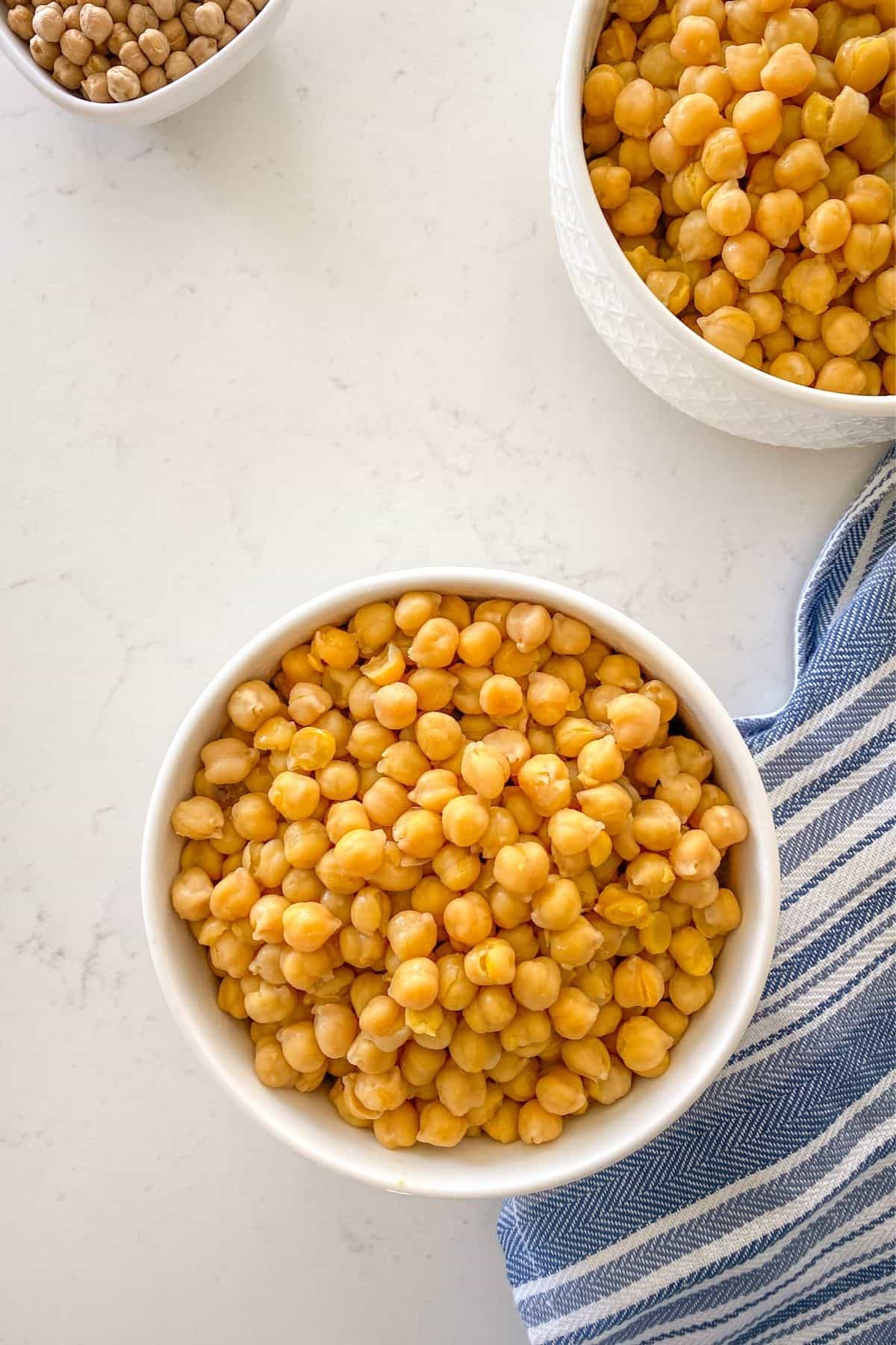 Two white bowls filled with chickpeas with blue and white dish cloth beside them.