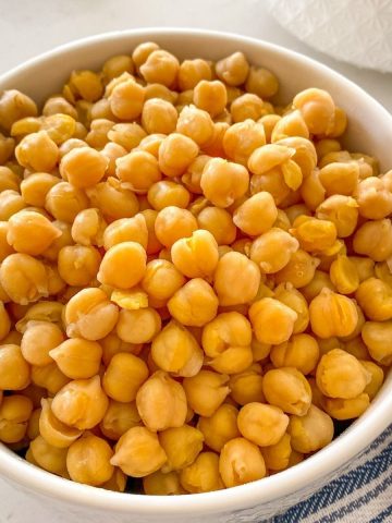 White bowl filled with cooked chickpeas and blue towel beside it.