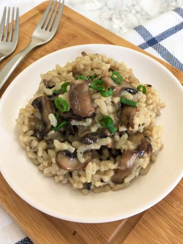 Mushroom risotto in white plate with green onion garnish.