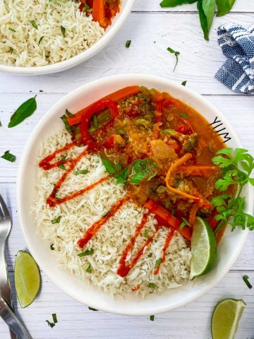 white bowl with rice, thai curry and drizzled in hot sauce
