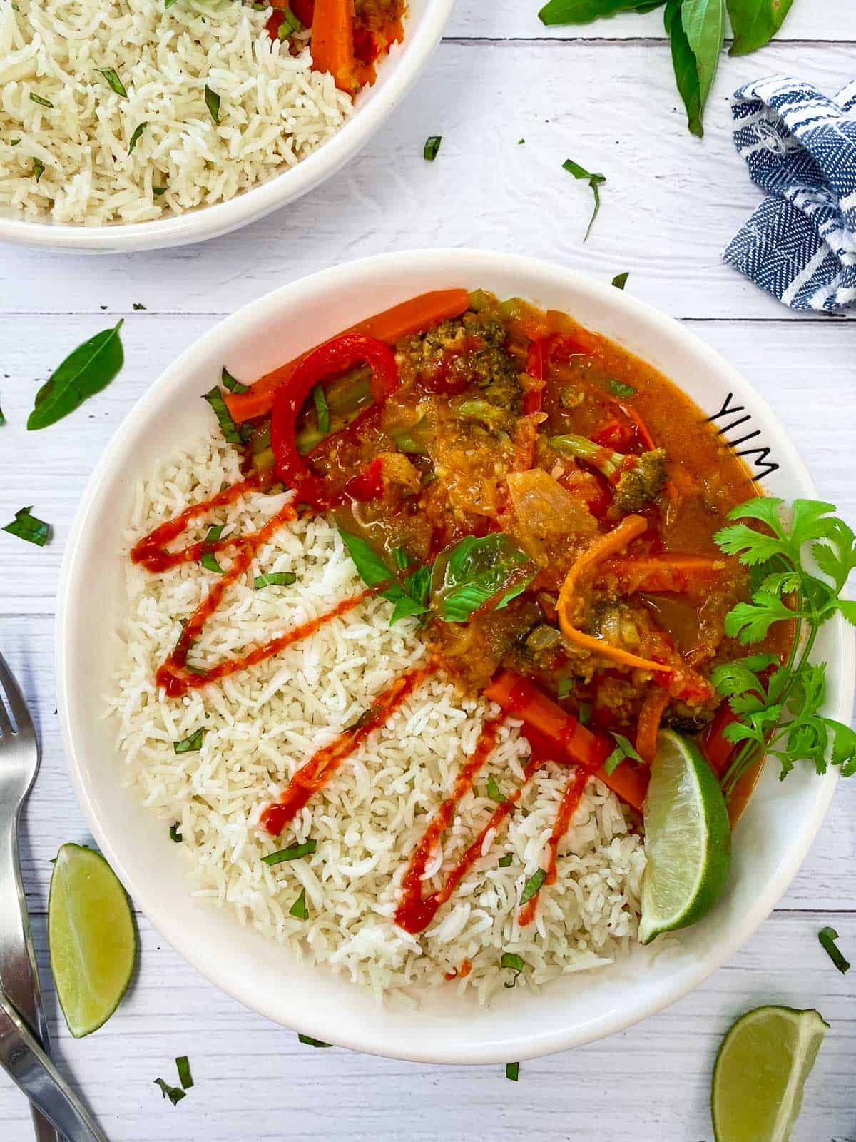 white bowl with rice, thai curry and drizzled in hot sauce