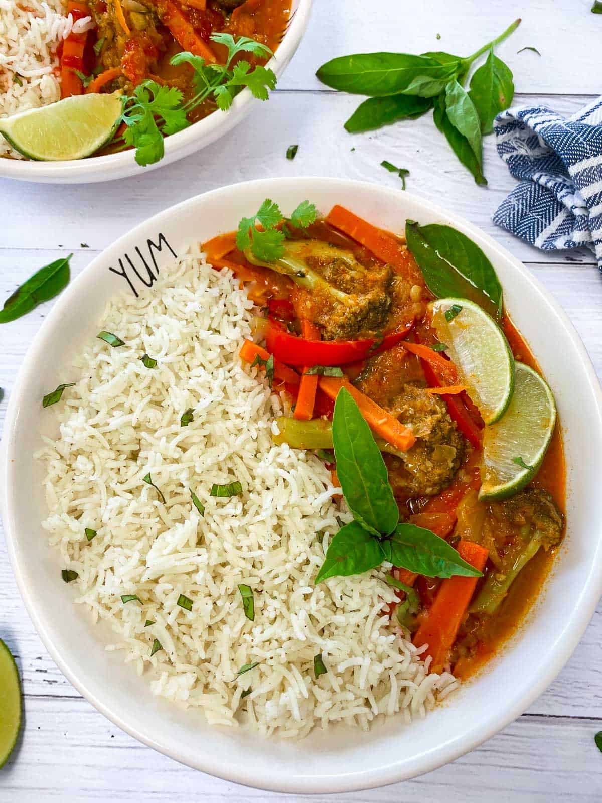 bowl of white rice and veggies with red thai curry sauce and garnished with lime wedges and basil
