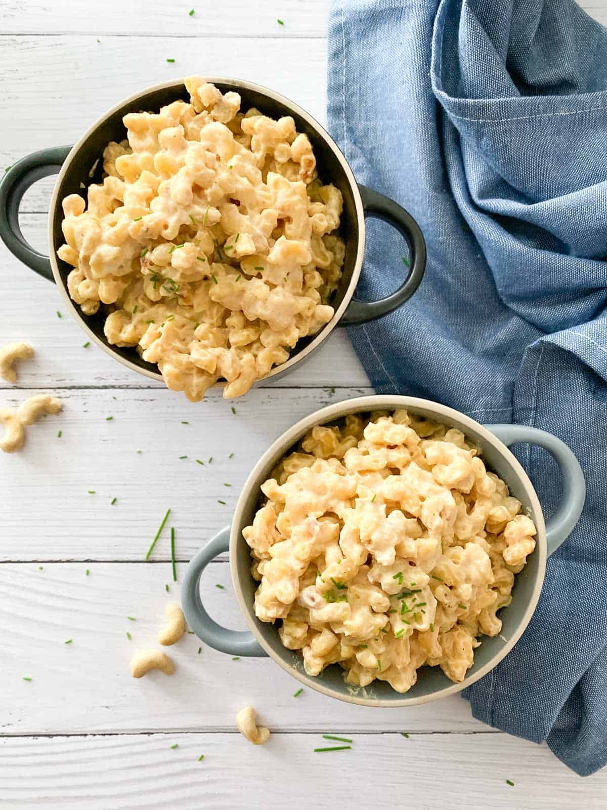 Two bowls of mac and cheese with chives garnish and blue dishcloth beside them.