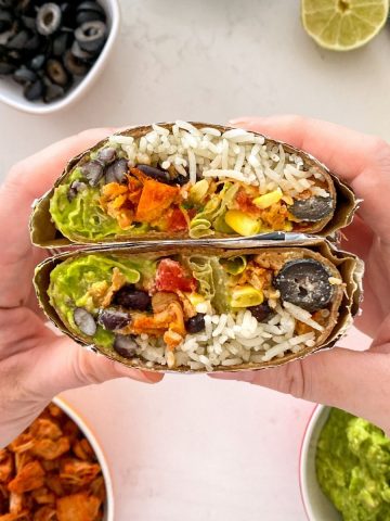 Hands holding up jackfruit burrito that is cut in half.