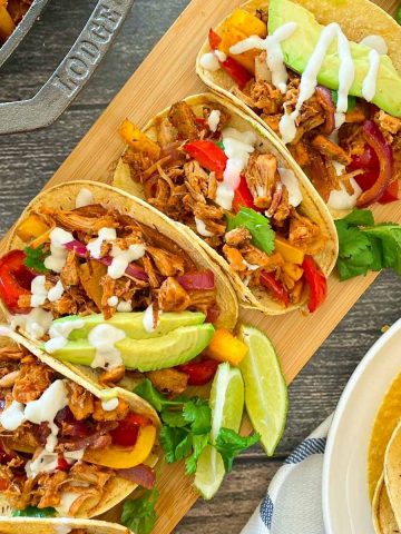 Cutting board with fajitas in corn tortillas with avocado, cilantro and crema fresca garnish.