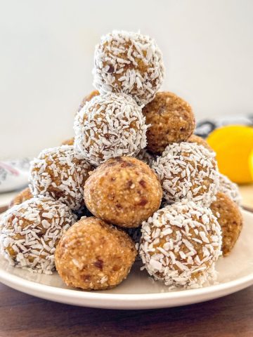 Lemon bliss balls stacked in a pyramid shape on white plate.