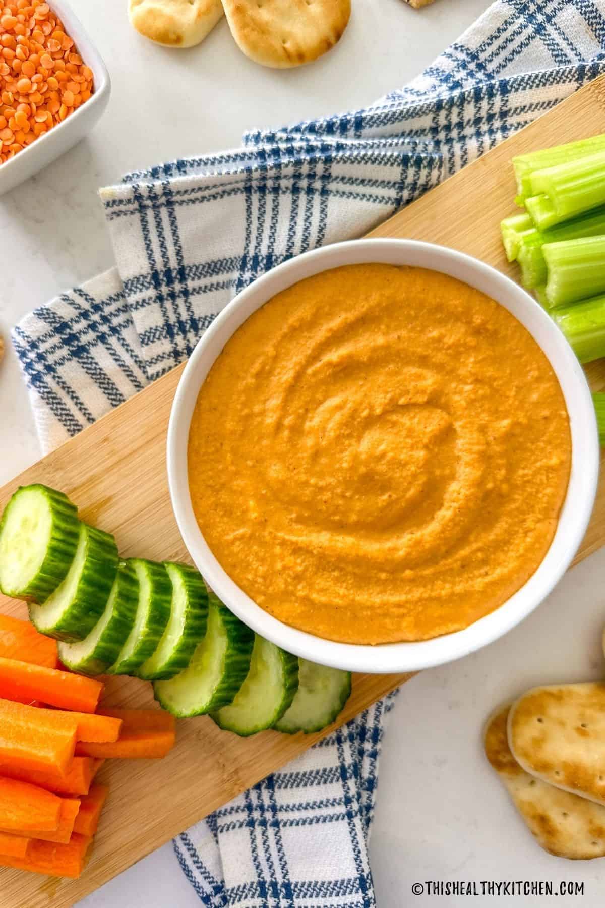 Bowl of lentil hummus on cutting board with veggies and pita bread around it.