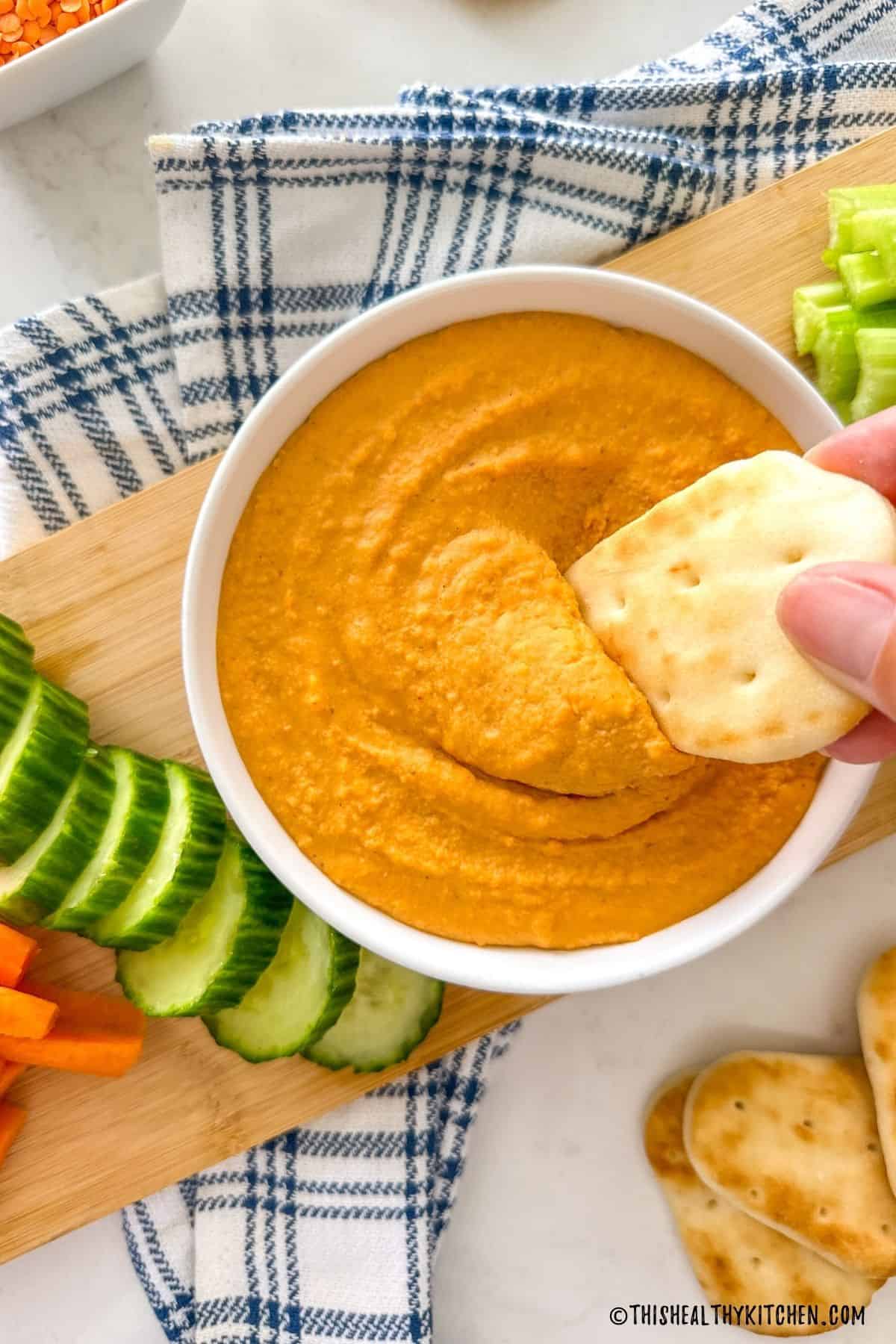 Pita bread being dipped into bowl of red lentil dip.