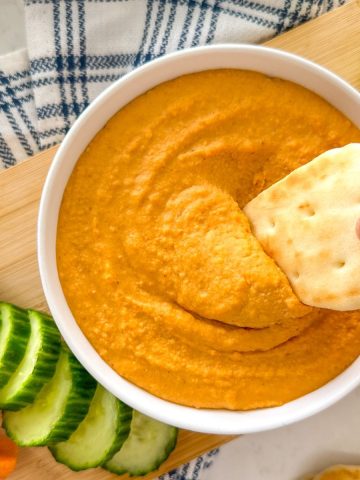 Pita bread being dipped into bowl of orange lentil dip.