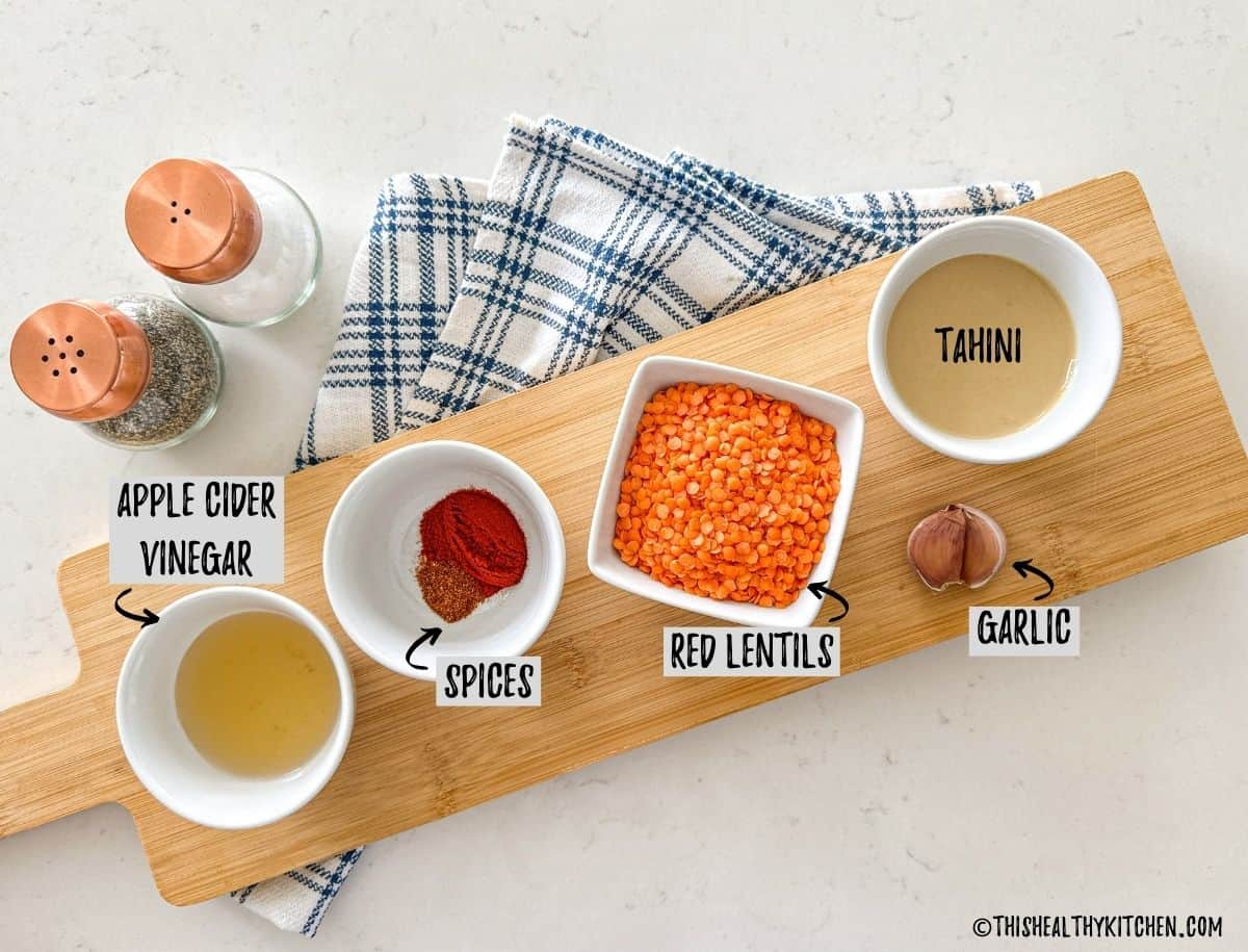 Bowls of lentils, spices, vinegar, tahini, and garlic on kitchen countertop.