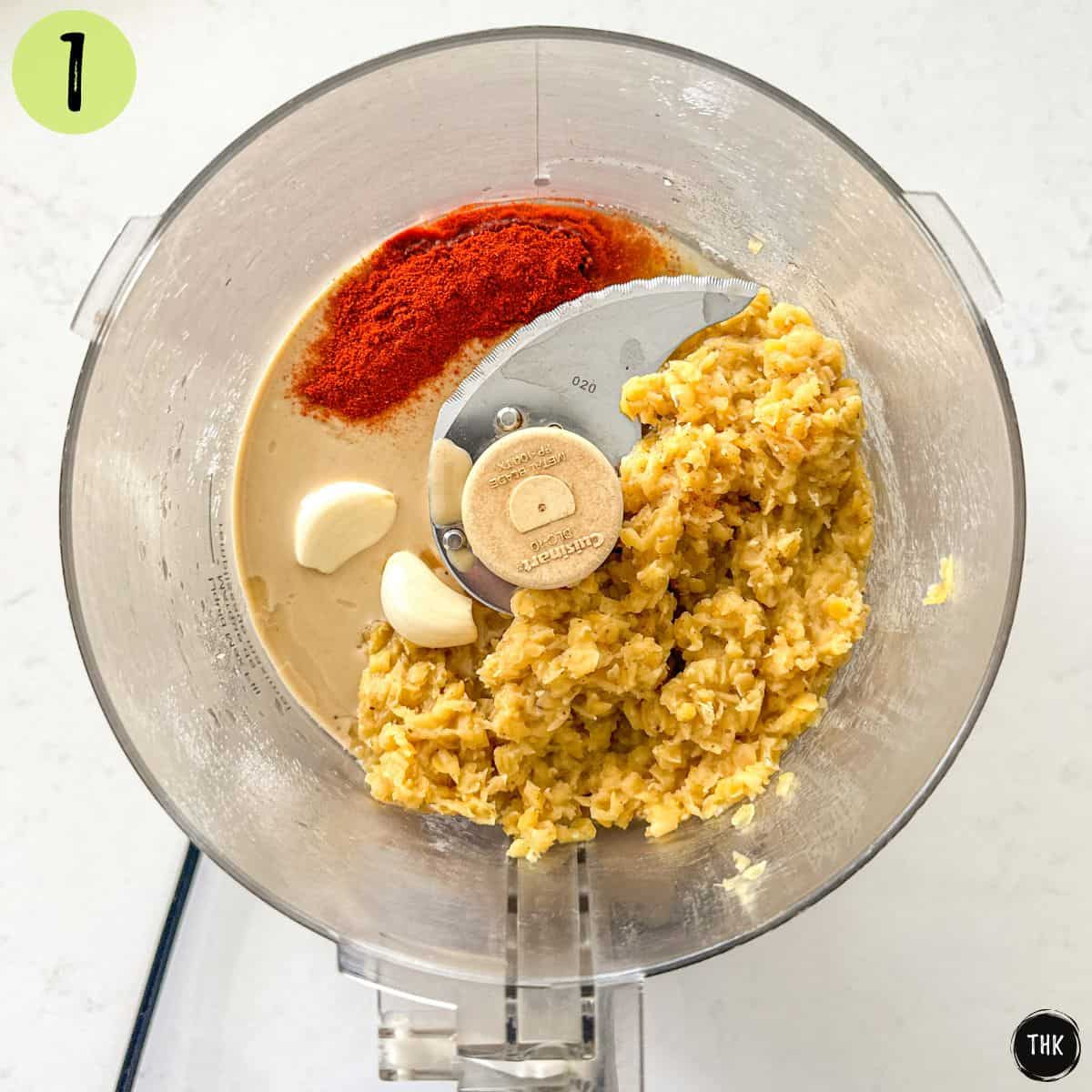 Food processor with cooked lentils, spices, garlic and tahini inside.