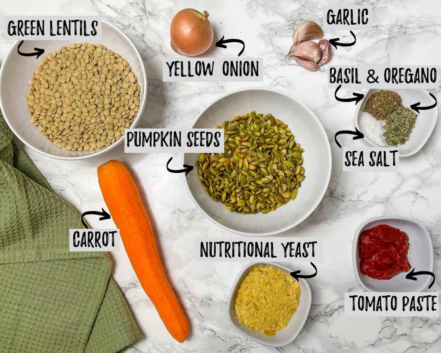 bowl of lentils, pumpkin seeds, nutritional yeast, seasoning, tomato paste, onion, garlic and carrot on marble counter