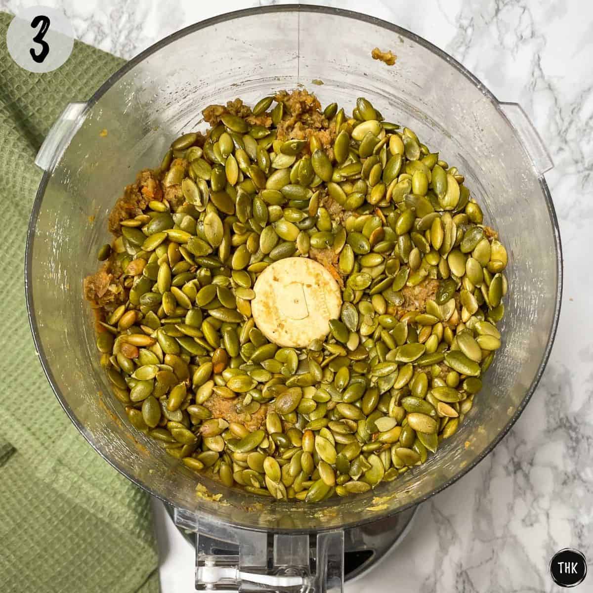 Pumpkin seeds on top of blended mixture in food processor.