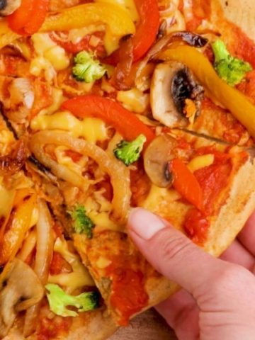 hand lifting slice of pizza from cutting board.