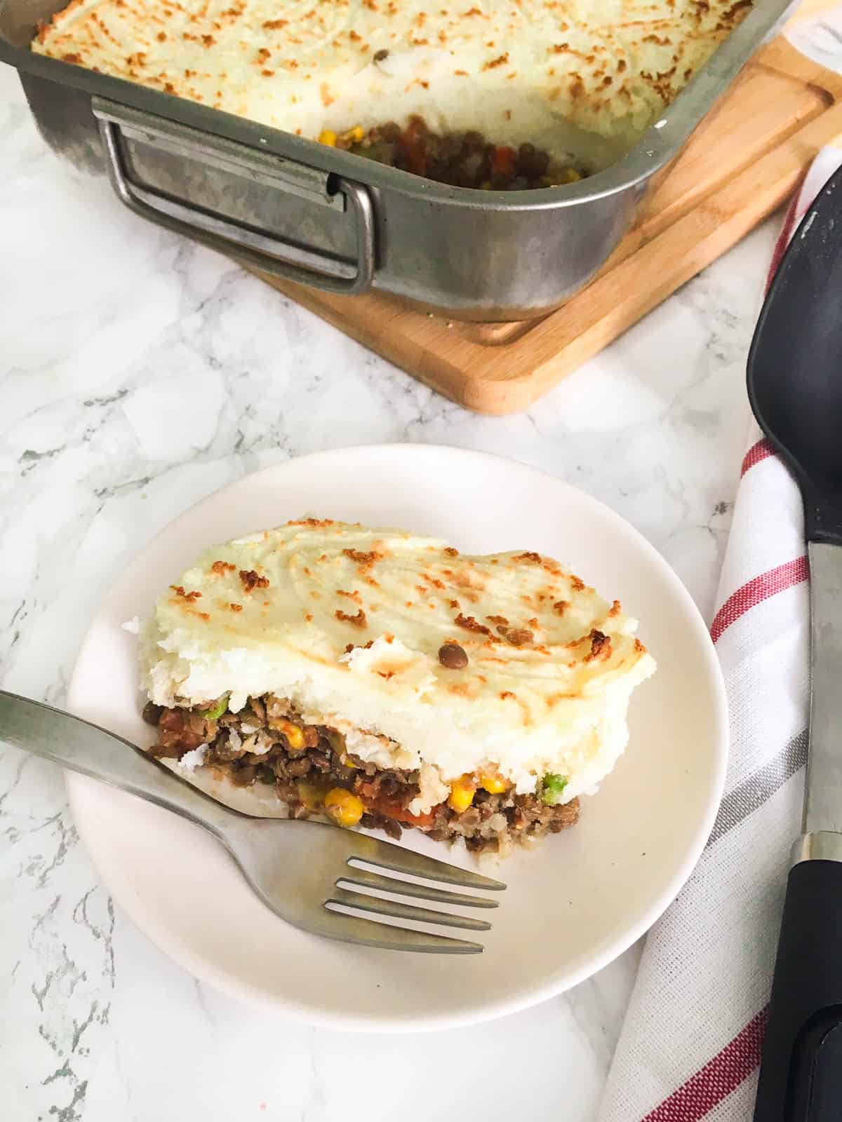 White plate with shepherd's pie in it and fork on the side of the slice.