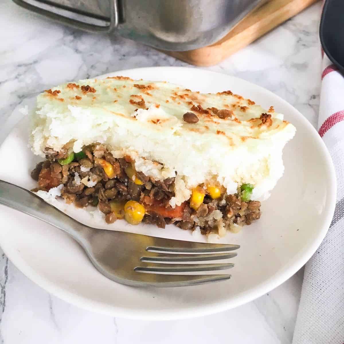 slice of lentil shepherd's pie in plate with fork.