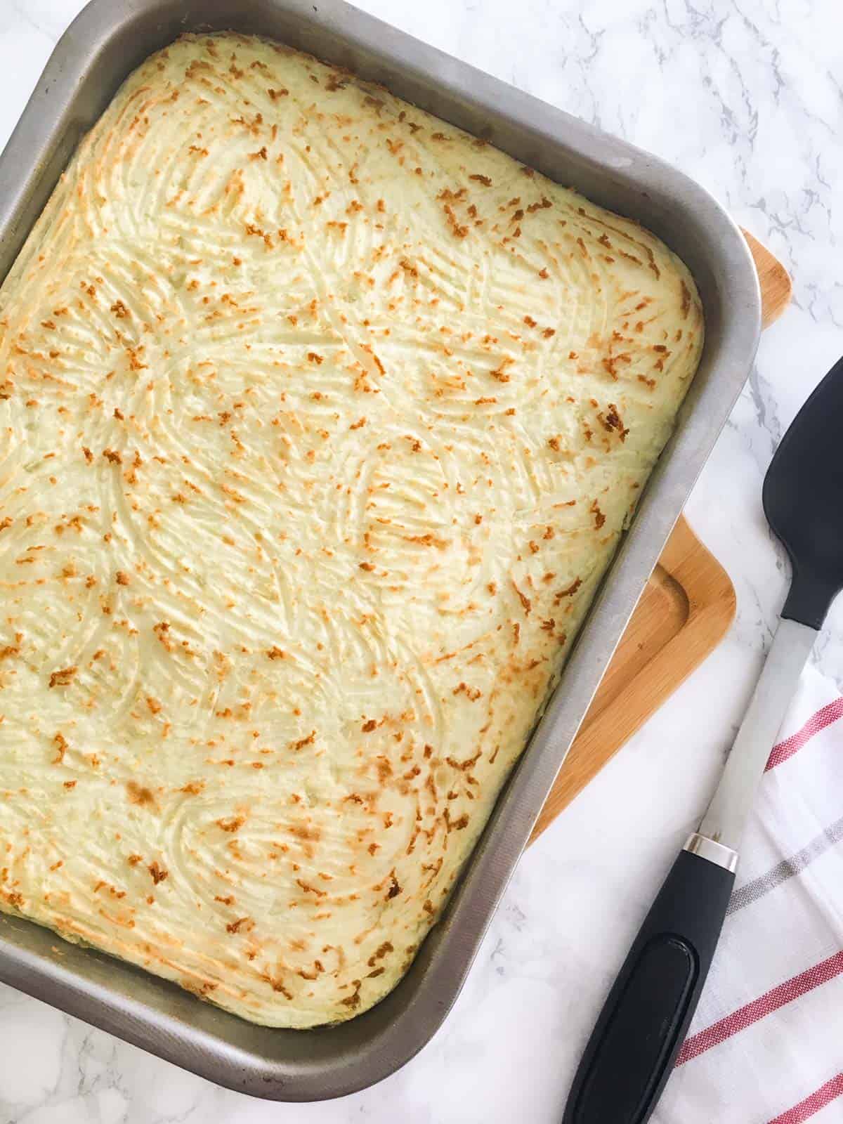 Lentil shepherd's pie in baking dish, fresh out of the oven resting on cutting board.