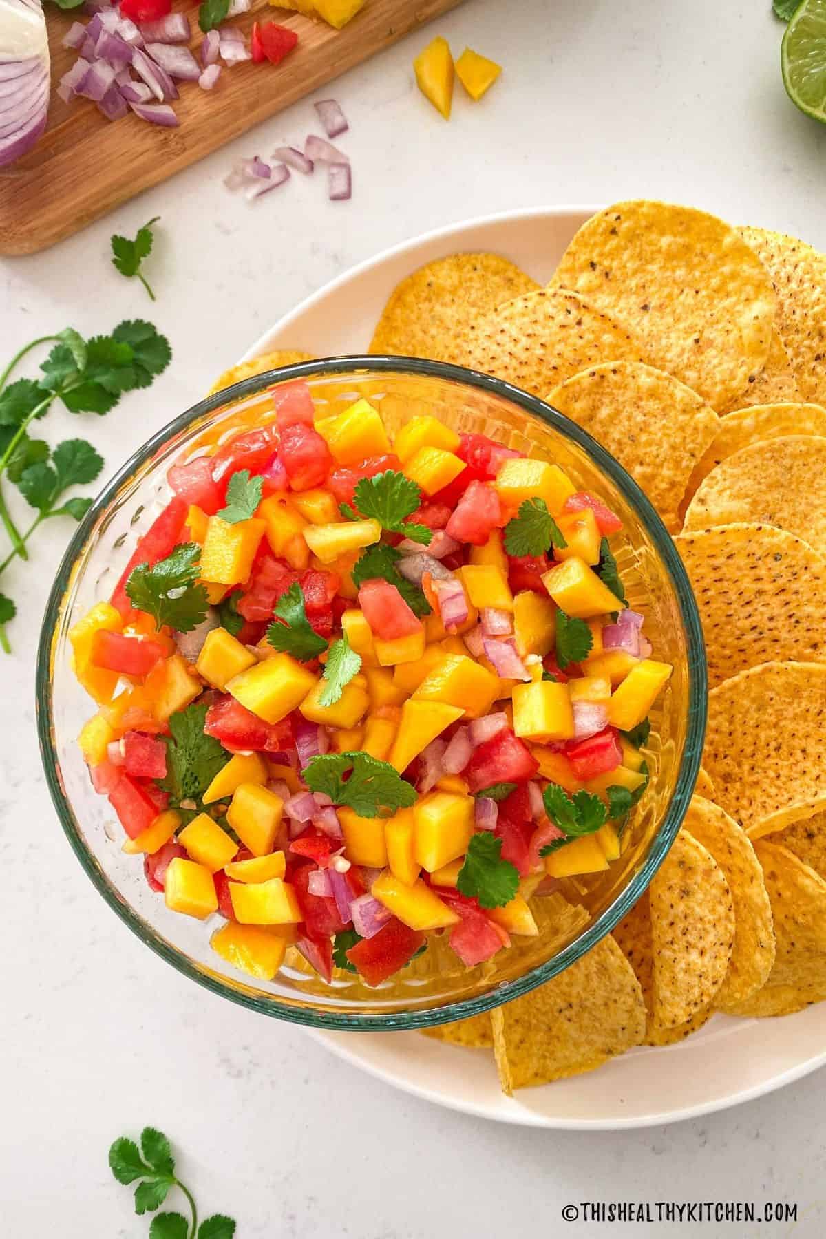 Glass bowl with mango habanero salsa inside on plate of chips.
