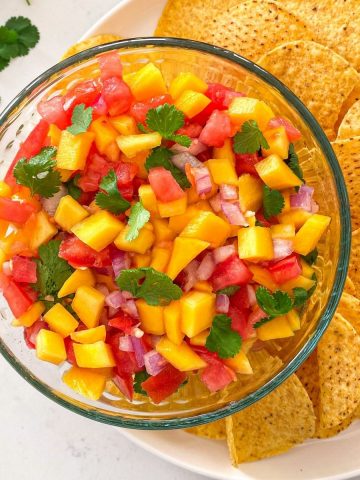 Glass bowl with mango habanero salsa inside on plate of chips.