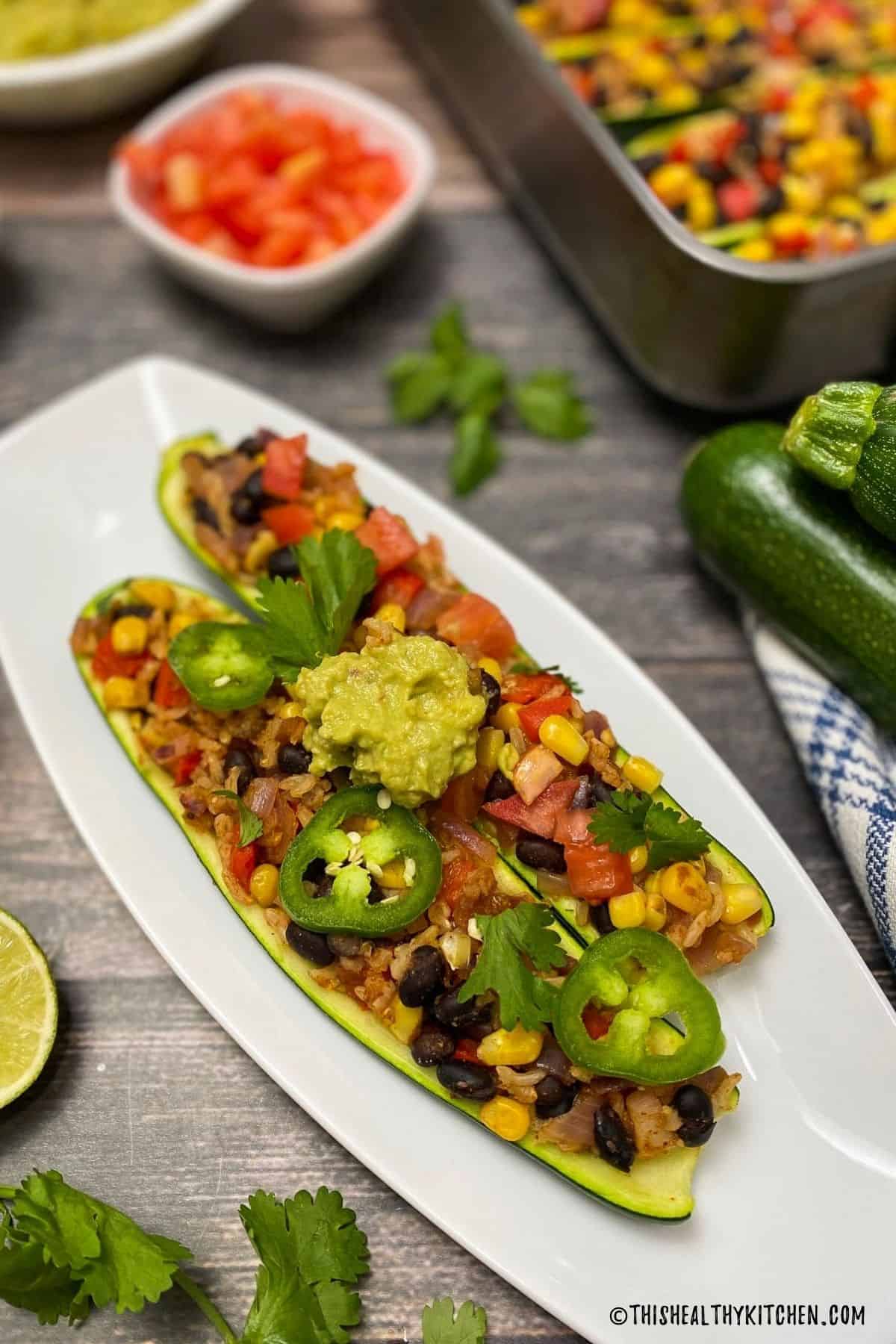 Two zucchini boats stuffed with rice, beans, corn, and topped with guacamole and jalapeno.