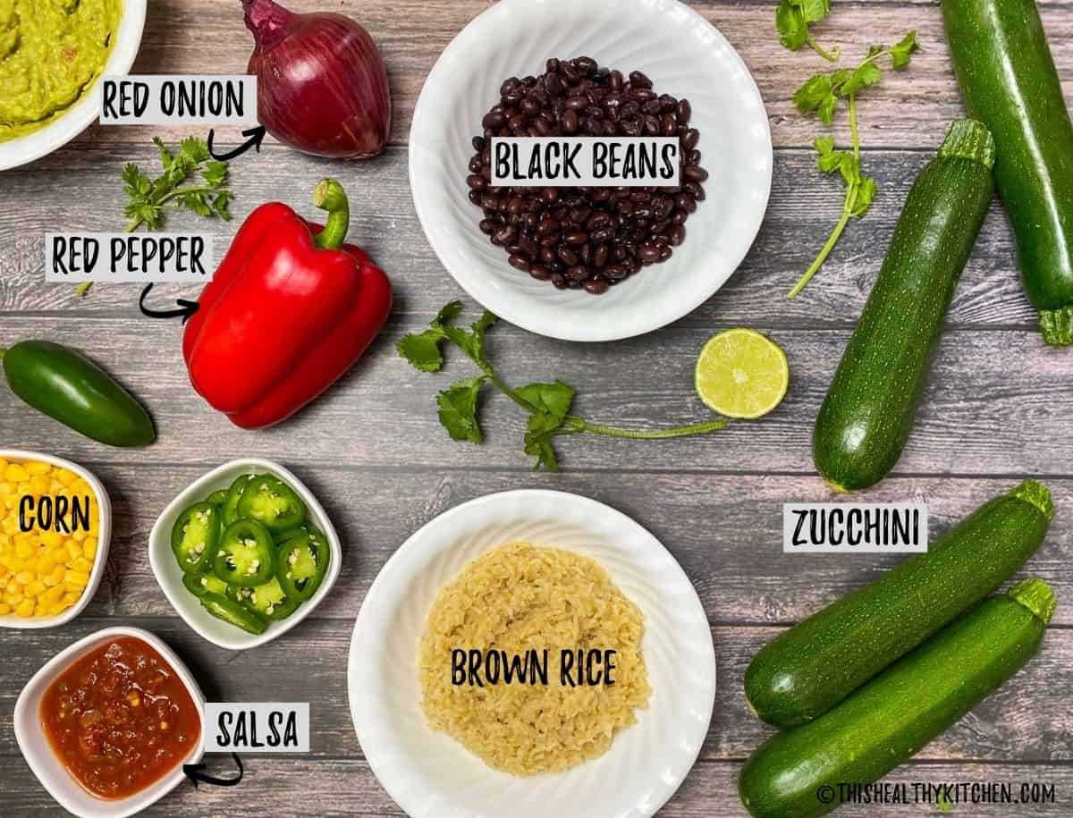 Zucchini, rice, black beans, pepper, onion, corn and salsa scattered on on brown deck.