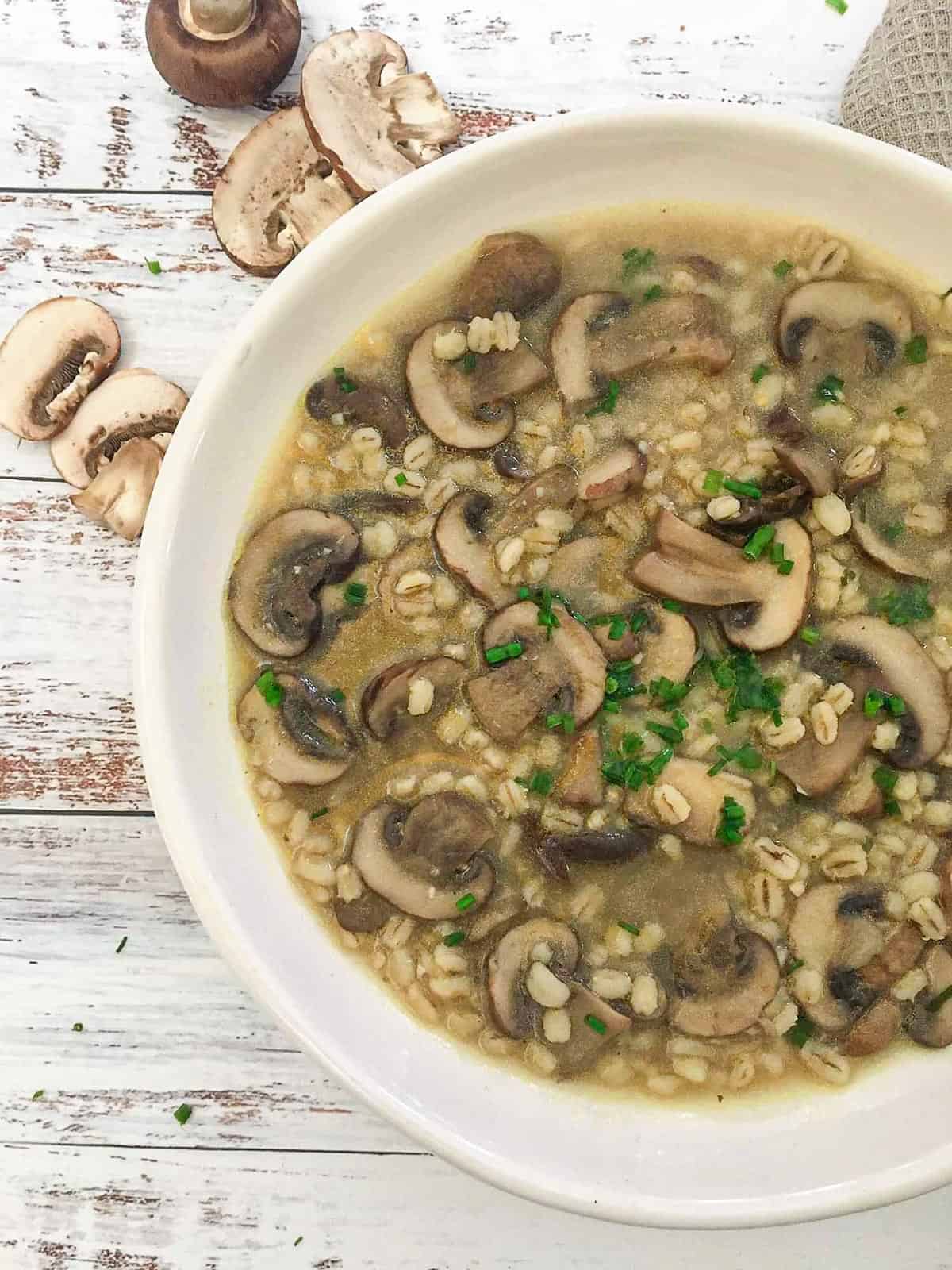 White bowl of mushroom barley soup with parsley garnish.