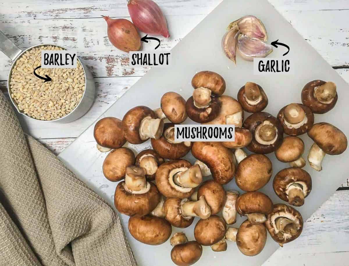 Mushrooms and garlic on cutting board with shallots and barley beside it.