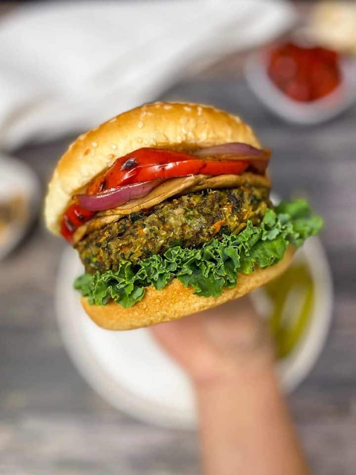 hand holding up veggie burger with lettuce, onion, and peppers inside