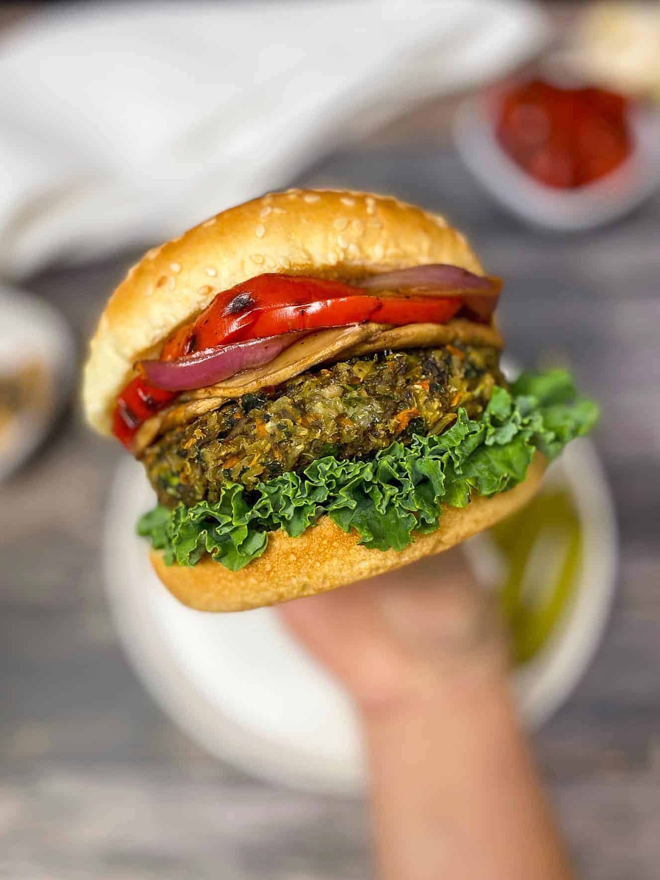 hand holding up veggie burger with lettuce, onion, and peppers inside