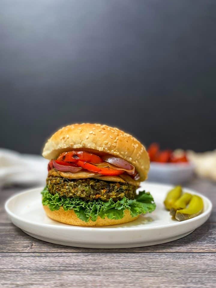 mushroom risotto burger in bun with lettuce, onion, peppers, on white plate with pickles on the side