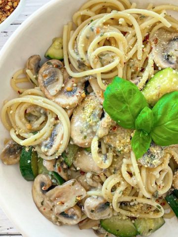 Plate of spaghetti, zucchini and mushrooms with basil on top.