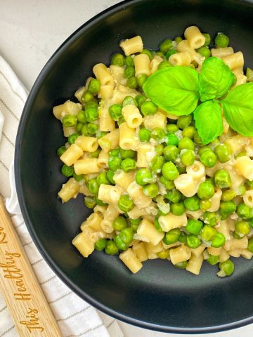 Black bowl with pasta and peas inside with basil leaf garnish.