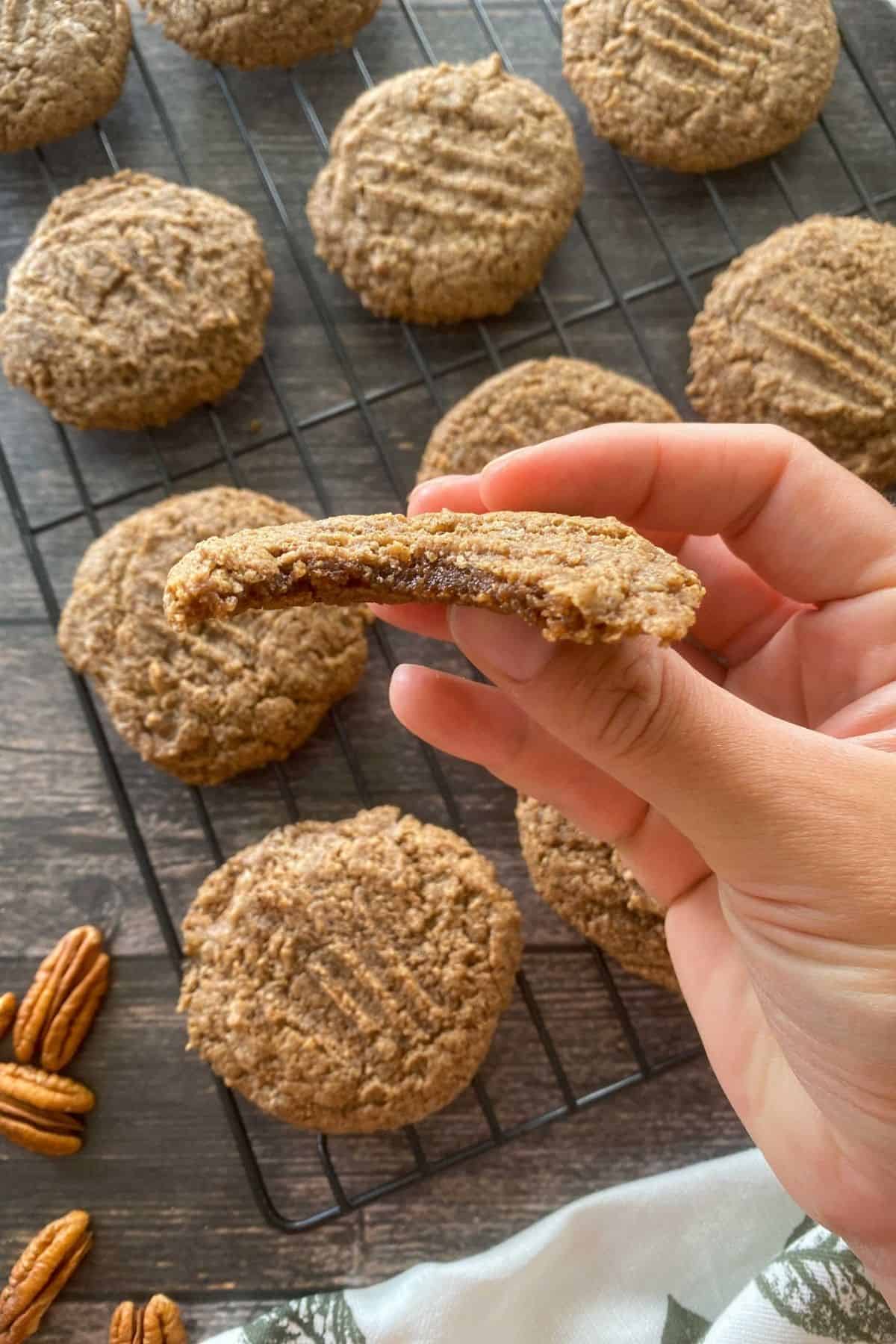 Hand holding up cookie above cooling rack of remaining cookies.