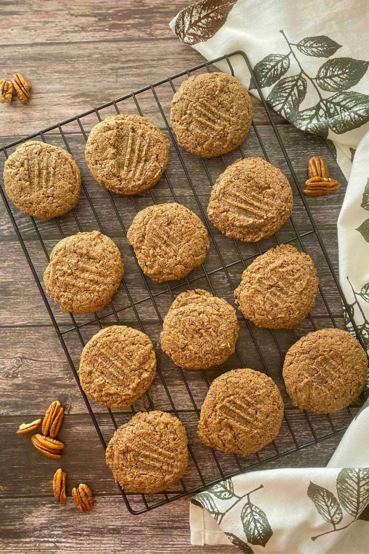 Cookies on cooling rack with pecans scattered around them on brown deck.