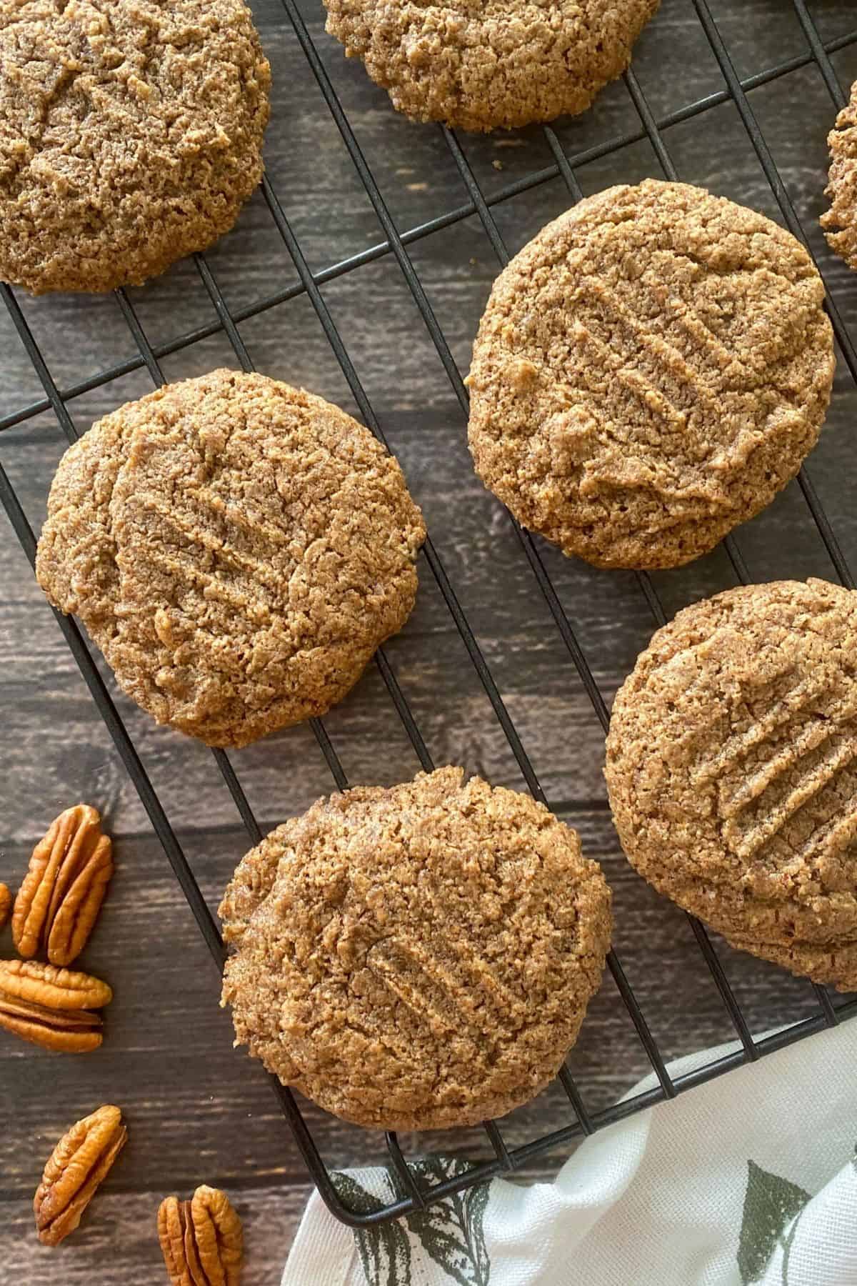 Cooling rack with pecan cookies on top and pecans on the side.