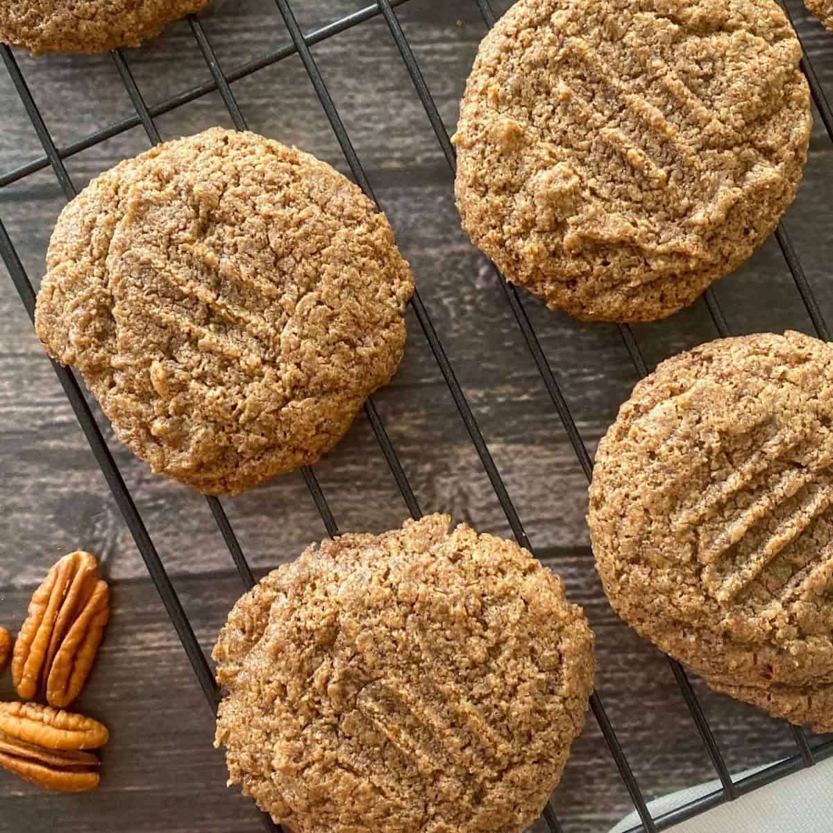 Cooling rack with pecan cookies on top and pecans on the side.