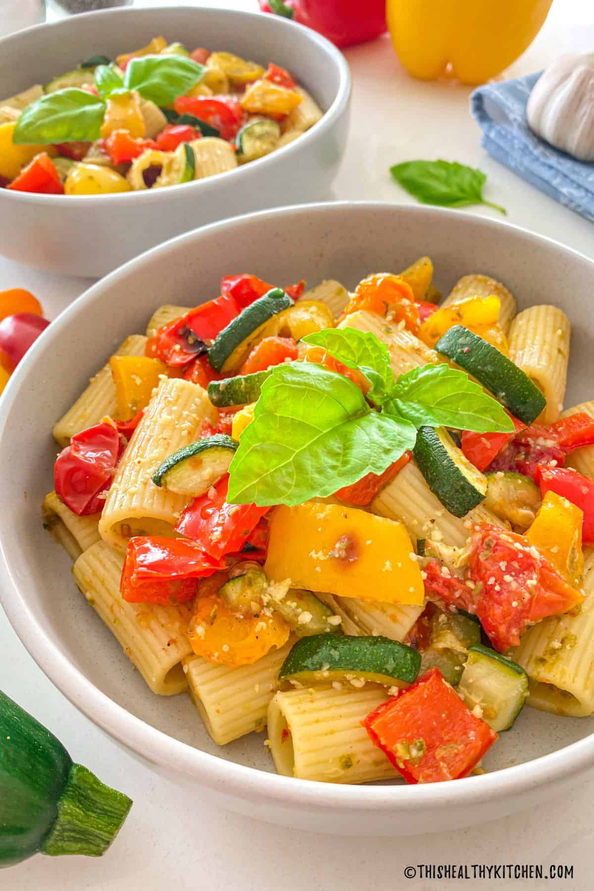 Side view of plates with pesto pasta and veggies inside.
