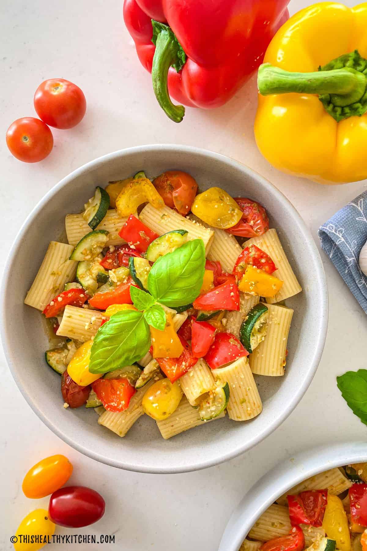 Grey bowl of pasta with pesto and roasted vegetables.