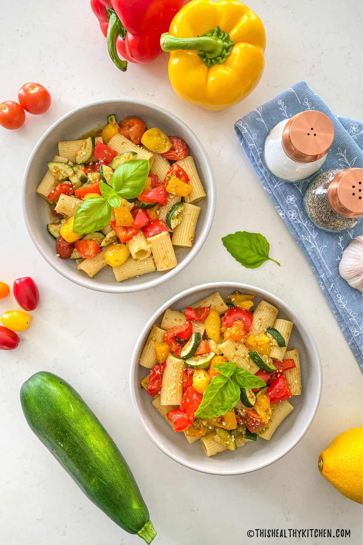 Two bowls with pasta, roasted veggies, and basil on top.