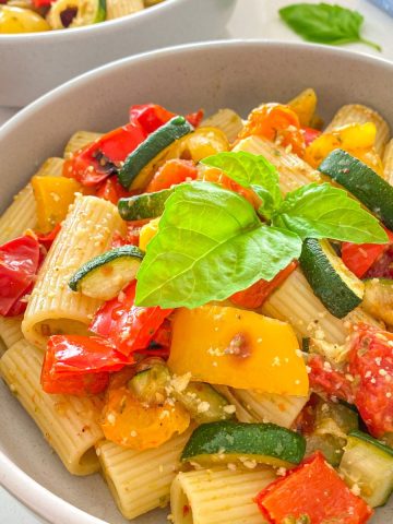 Side view of plates with pesto pasta and veggies inside.