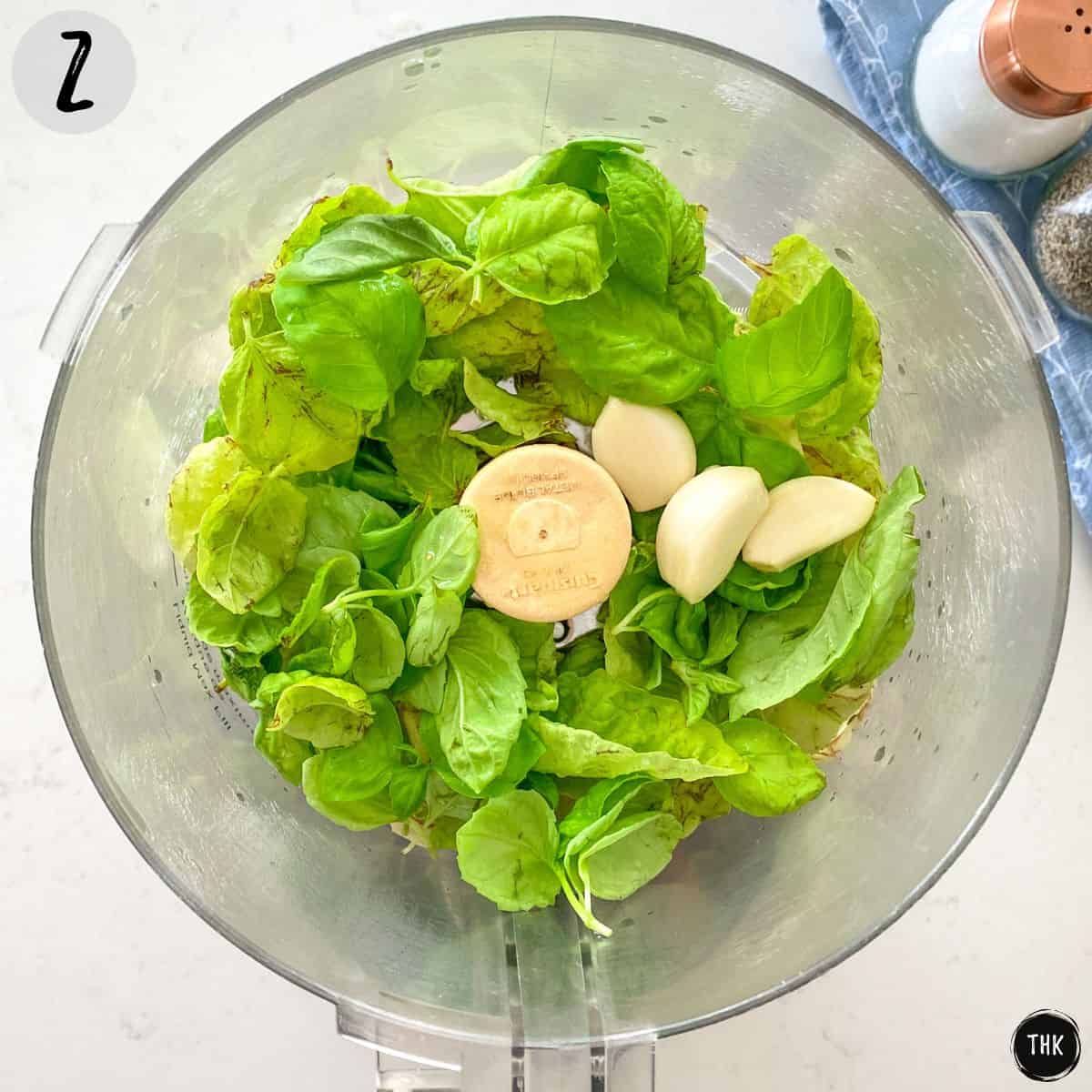 Food processor bowl filled with basil leaves, garlic and lemon juice.