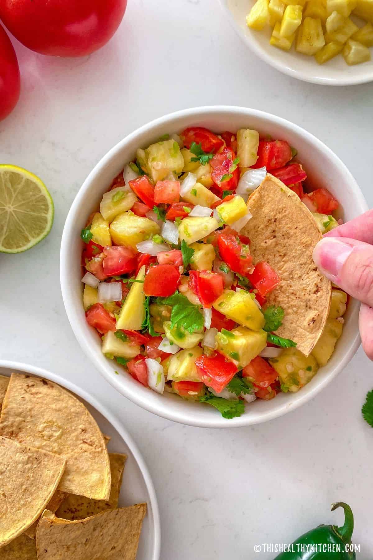 Hand dunking chip into bowl of salsa.