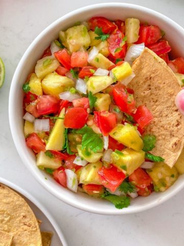 Hand dunking chip into bowl of salsa.