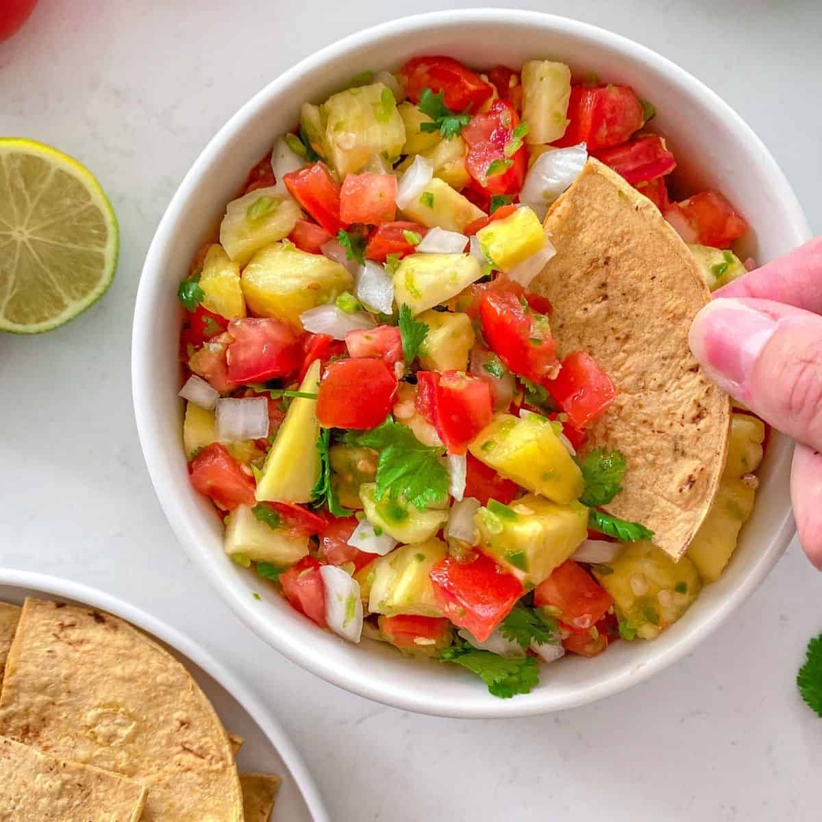 Hand dunking chip into bowl of salsa.